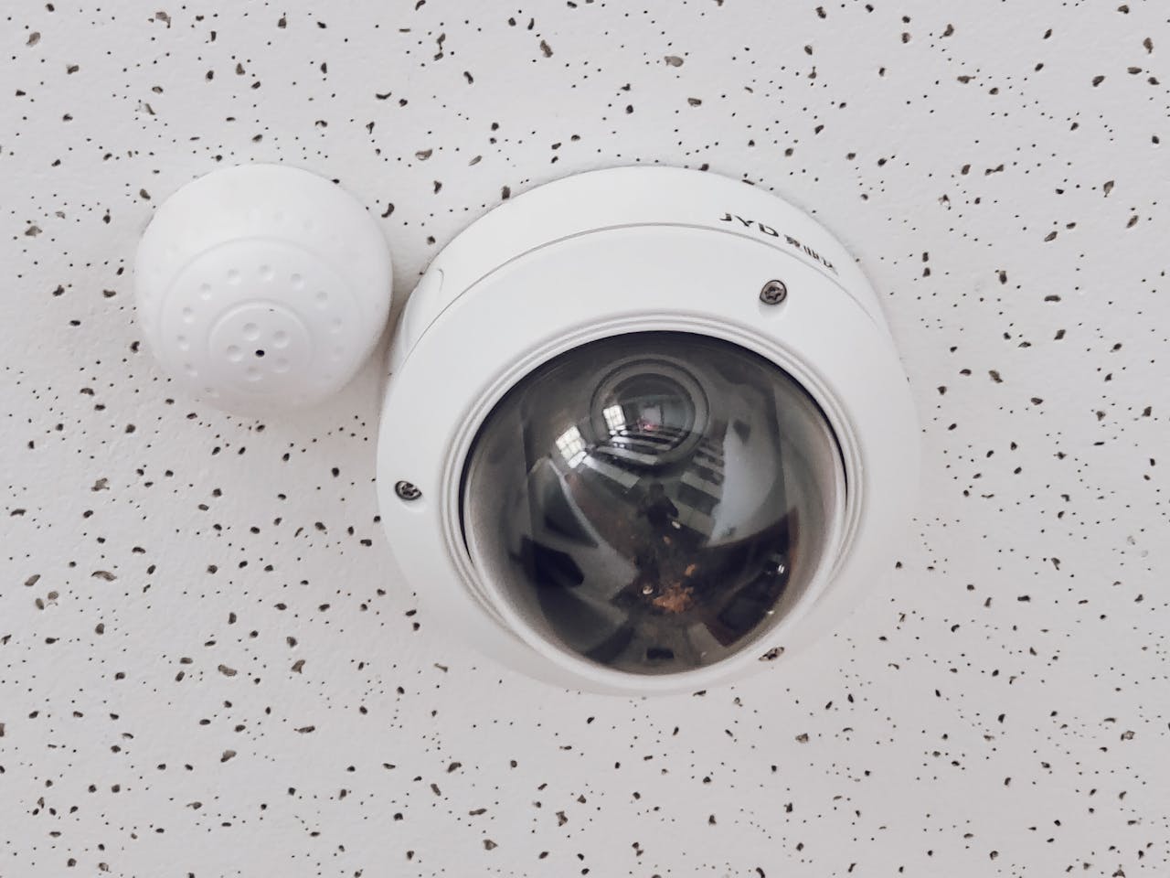 Services Close-up of a round dome surveillance camera installed on a speckled ceiling for security monitoring.